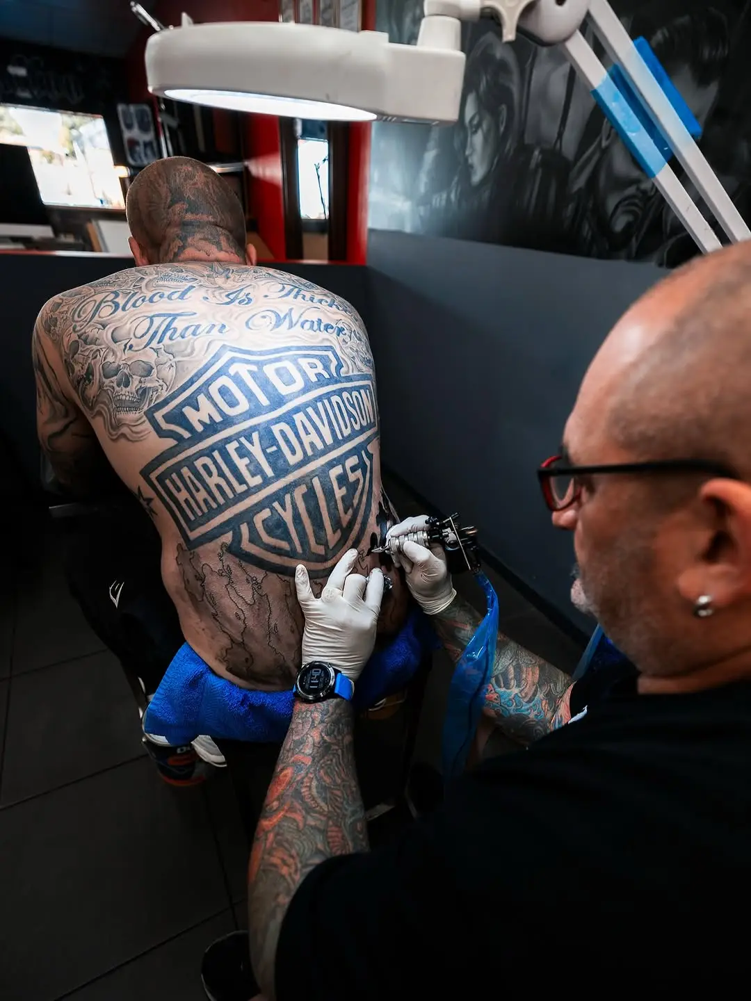 An artist shading the lower section of a black and grey back piece, seen over their shoulder