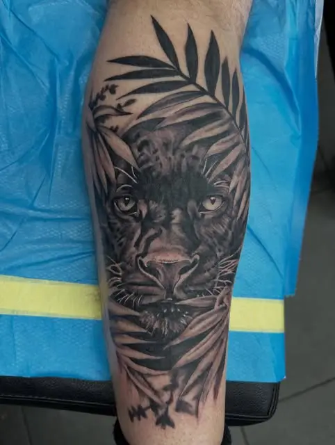 A black and grey panther looking through palm fronds, tattooed on a calf